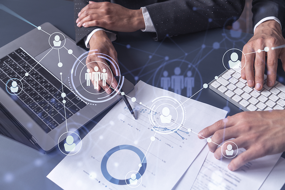 two people's hands pointing to figures on paper with a laptop open in the background and a graphic of an employment chart superimposed